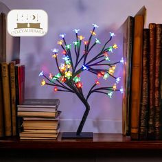 a lighted tree is sitting on a book shelf next to some books and a pile of books