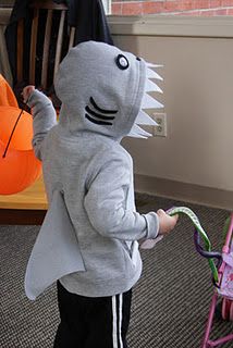 a little boy in a shark costume standing next to a child's stroller