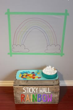 a wooden box sitting on top of a hard wood floor next to a wall with a rainbow drawn on it