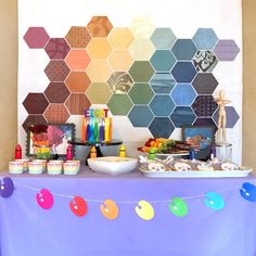 a table topped with lots of food next to a wall covered in hexagonal tiles