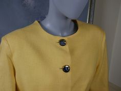 This 1990s Italian vintage short-sleeve summer blazer is a beautiful yellow color, and is crafted from a woven viscose that gives the appearance of fine linen. The professional jacket has a round neckline and padded shoulders, and closes in the front with five black and gold buttons. One black and gold button decorates each sleeve edge. The blazer features figure-enhancing contour lines on the front and the back, and has a fitted waistline that then falls with a slight flare. The jacket is lined Yellow Formal Blazer With Buttons, Summer Yellow Blazer For Workwear, Summer Workwear Yellow Blazer, Formal Yellow Blazer With Buttons, Yellow Summer Blazer For Work, Summer Yellow Blazer For Work, Yellow Formal Summer Blazer, Summer Formal Yellow Blazer, Yellow Buttoned Blazer For Spring