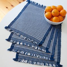 a bowl of oranges sitting on top of a blue and white table cloth next to a bowl of oranges