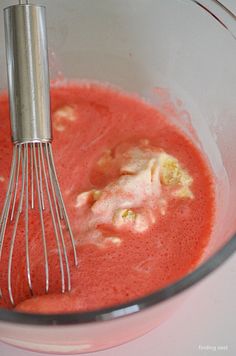 a whisk in a bowl filled with red liquid and other things to make it look like food