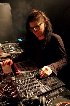 a man with long hair and glasses working on some electronic equipment