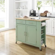 a green kitchen island with wooden top in the middle of a wood floored kitchen