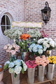 a bunch of vases filled with flowers sitting on top of a wooden table next to a brick wall