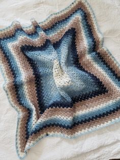 a crocheted blanket on top of a bed next to a white sheet and pillow