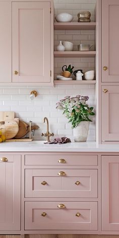 a kitchen with pink cabinets and white tile backsplash, brass pulls on the cupboards