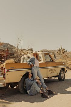 two people sitting on the back of a pickup truck in the middle of an arid area