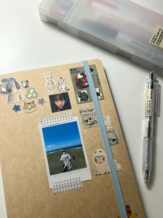 an open notebook with various stickers and pictures on it, next to a pen