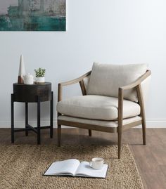 an open book is sitting on the floor next to a chair and table with a vase