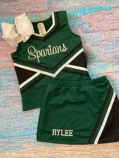 two green cheer uniforms with white letters on the front and black bottom, one has a bow at the back