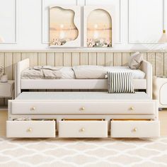 a white daybed with drawers underneath it in a room that has two pictures on the wall