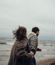 two people are walking along the beach with their hands in each other's pockets