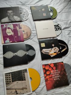 various records are laying on a bed with white sheets and black and yellow discs next to them