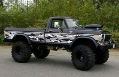 a black truck with camo paint job parked in front of some trees and bushes