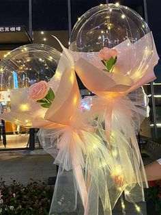 two clear bubble balloons with roses on them in front of a building at night time