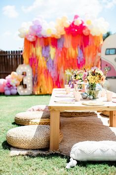 a picnic table set up with flowers and balloons in the background for a birthday party