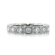 a white gold ring with four princess cut diamonds on the sides and an intricate band