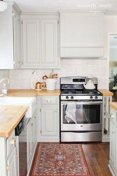 a kitchen with white cabinets and an area rug on the floor in front of the stove