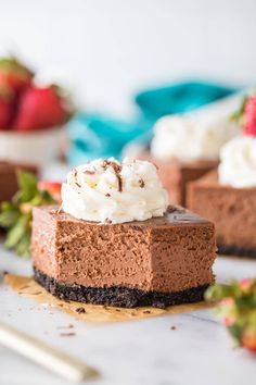 a slice of chocolate cheesecake with whipped cream on top and strawberries in the background