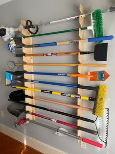 a wall mounted rack filled with different types of gardening tools and brooms on it