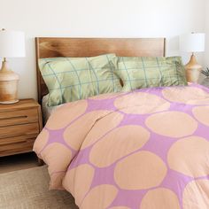 a bed with pink and green polka dot comforter on it, next to two nightstands