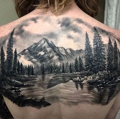 the back of a man's shoulder with a mountain scene and trees on it