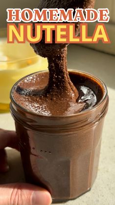 a hand is dipping chocolate into a jar with the words homemade nutella in it