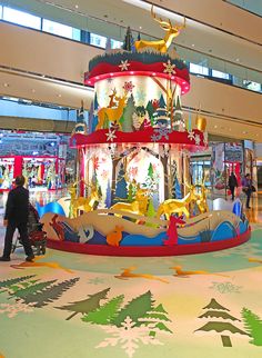 people are walking around an indoor carousel in the mall with christmas decorations and lights on it