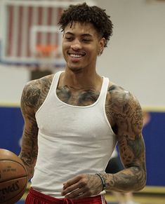 a man with tattoos holding a basketball in his hand and smiling at the camera while wearing red shorts