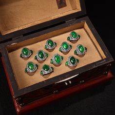 an open wooden box with seven green rings in it's display case on a black surface