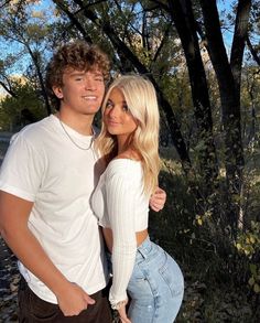 a young man and woman are posing for a photo in front of some trees with their arms around each other