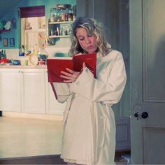 a woman standing in a kitchen holding a red binder and looking at the camera