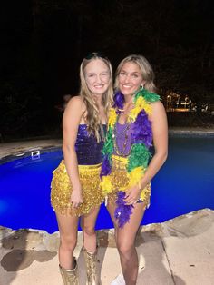 two women in costumes standing next to a swimming pool at night with their arms around each other