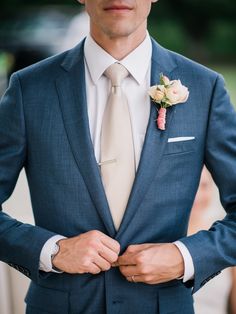 a man in a blue suit and tie with his hands on his chest, wearing a flower boutonniere