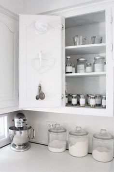 a kitchen with white cupboards filled with jars and containers next to a blender