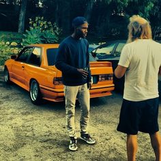 a man standing in front of an orange car