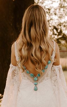 the back of a woman's wedding dress, with long hair and turquoise beads