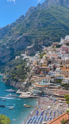 the beach is lined with umbrellas and boats in the water near some buildings on top of a mountain