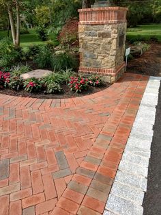 a brick walkway with flowers and trees in the background