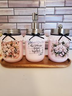 three jars with flowers on them sitting on a counter next to a soap dispenser