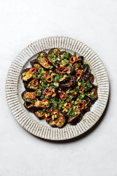 a white plate topped with eggplant, peppers and other toppings on top of a table