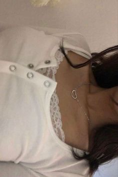 a woman in white shirt laying on top of a bed wearing a choker necklace