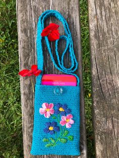 a crocheted bag with flowers on it sitting on a wooden bench next to a red flower