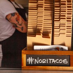 a person standing behind a wooden box with food in it that says nolitacos