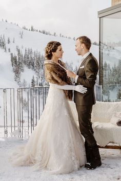 a bride and groom standing in the snow near a ski lodge looking into each other's eyes