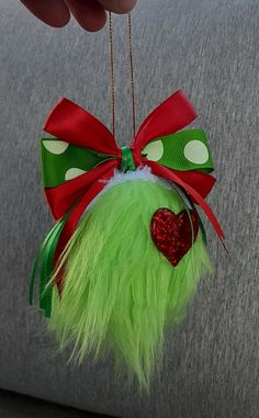 a hand holding a green ornament with a red heart on it's side