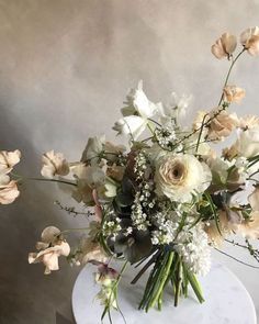 a vase filled with white flowers sitting on top of a marble table next to a wall