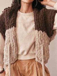 a woman with curly hair wearing a brown and white knitted jacket over her shoulders